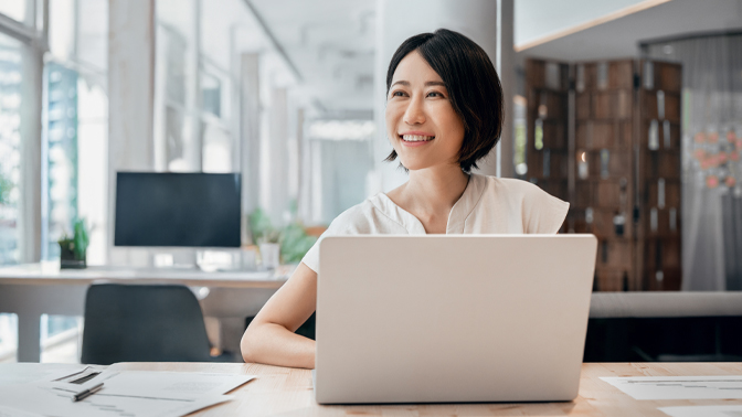 Woman sitting at table with laptop open smiling looking off in distance